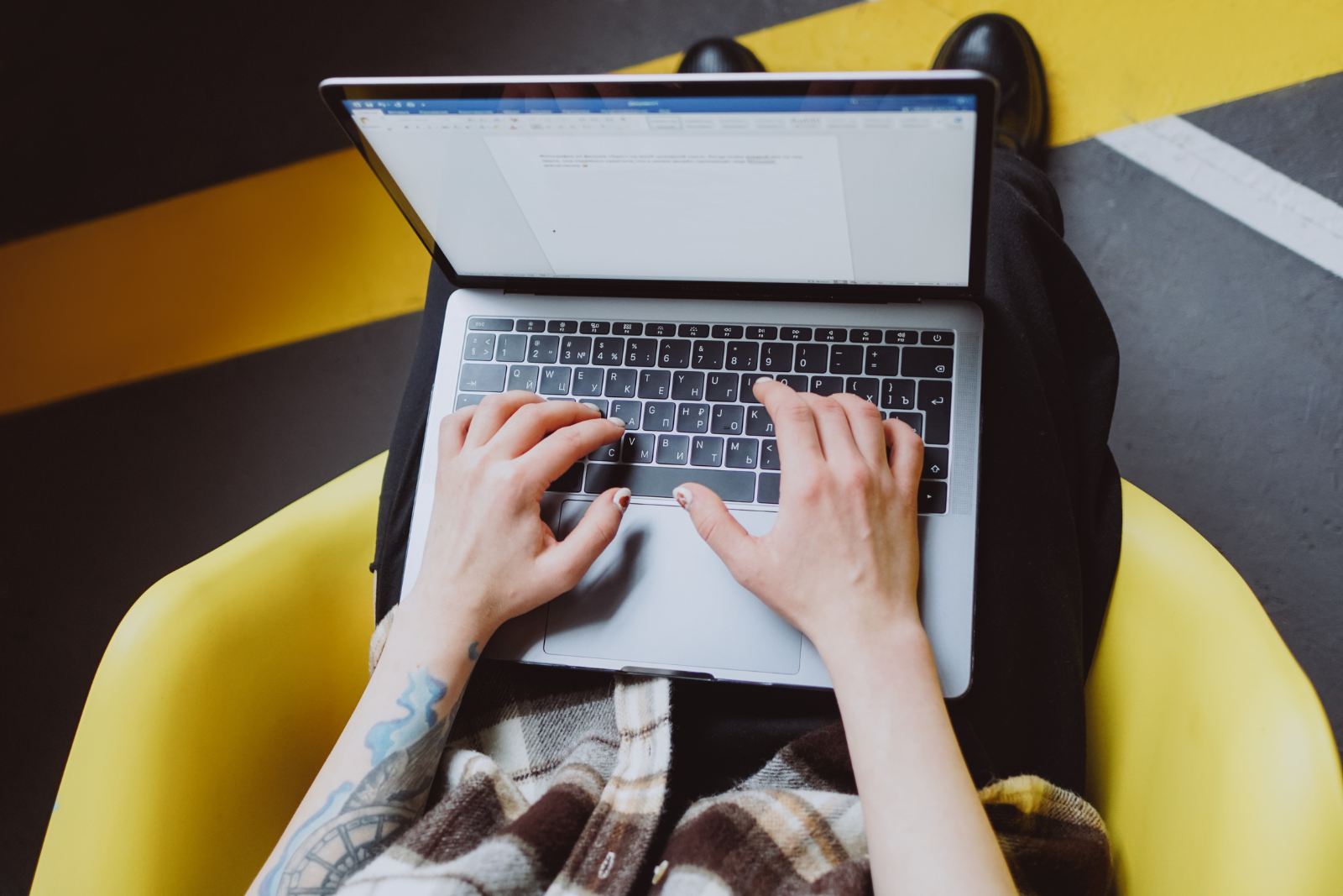 Man with tattoos typing a word document on a laptop that is sitting on his lap