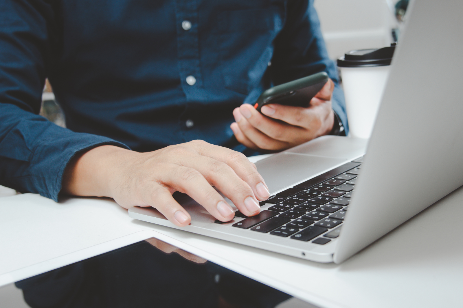 Man in a blue shirt in front of a open laptop with a phone in his hand